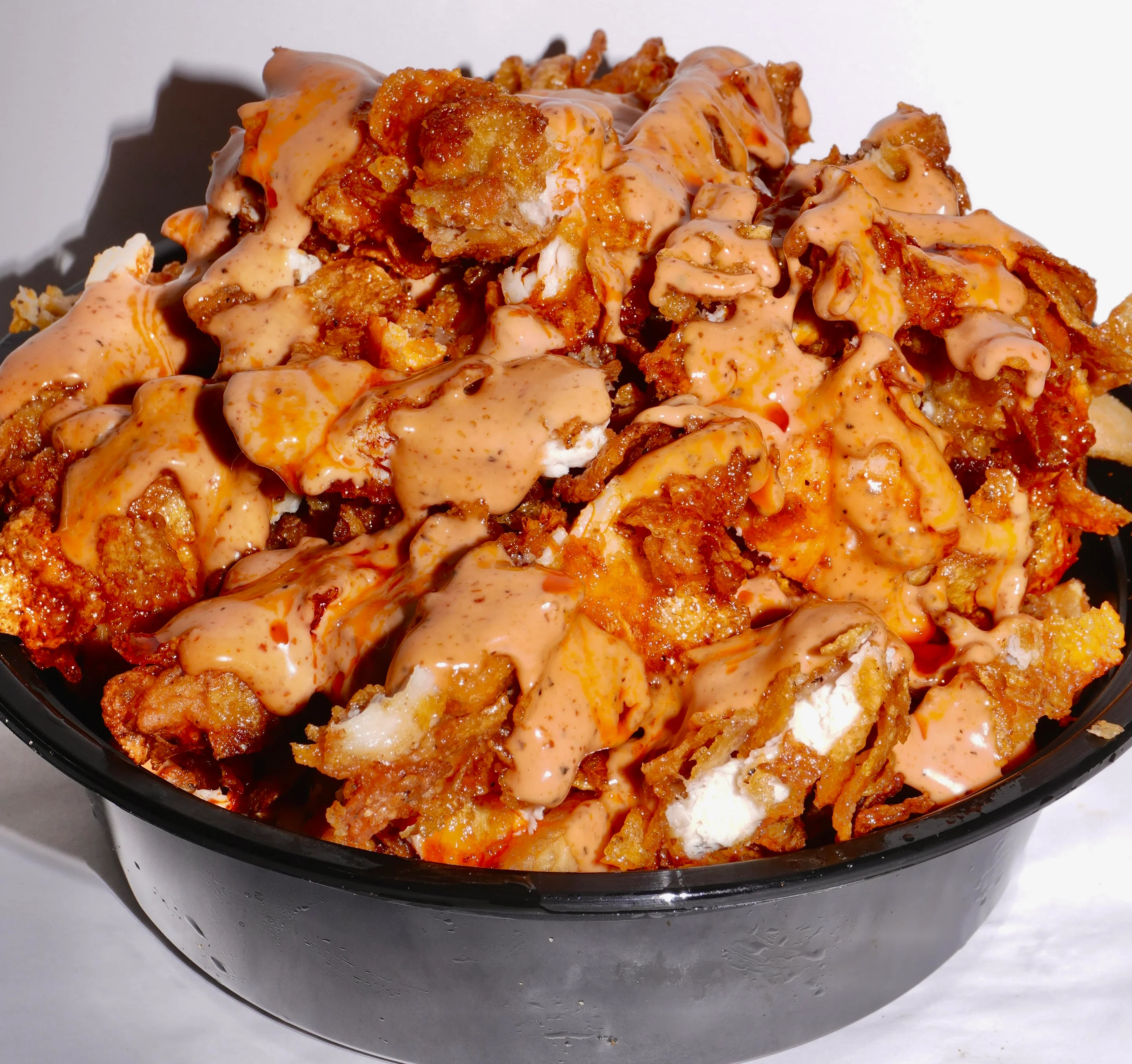 A bowl of loaded fries topped with meat, cheese, and spicy sauce, accompanied by two small sauce containers.