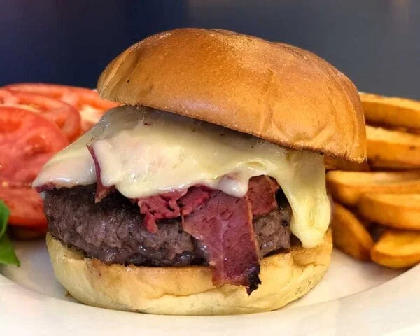 A delicious hamburger featuring a beef patty topped with melted cheese and sliced roast beef, accompanied by side slices of tomato and French fries.