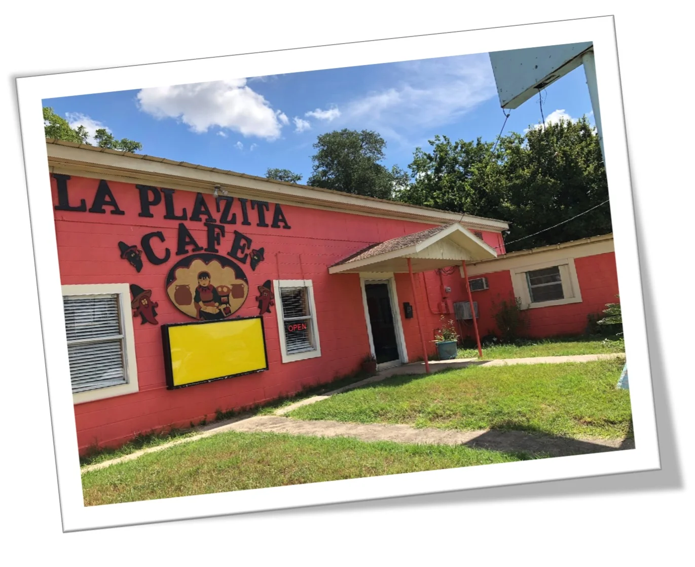 An exterior view of a brightly colored café named 'La Plazita'. The building is painted pink, with decorative elements and a welcoming entrance.