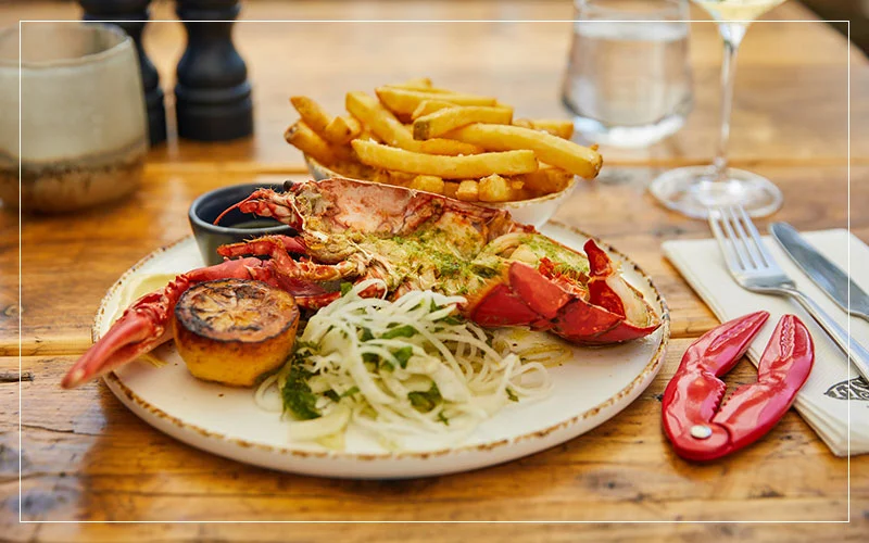 Grilled lobster with fries, salad, and a side of dipping sauce on a wooden table.