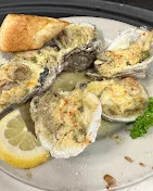 Oysters topped with a golden crust, served with a slice of lemon and a piece of toasted bread on a plate.