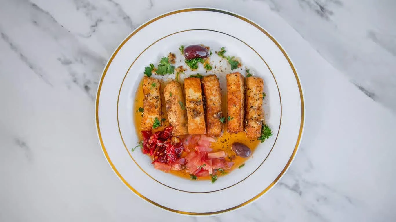 A plate featuring grilled sticks of a savory meat served with diced tomatoes, herbs, and olives.