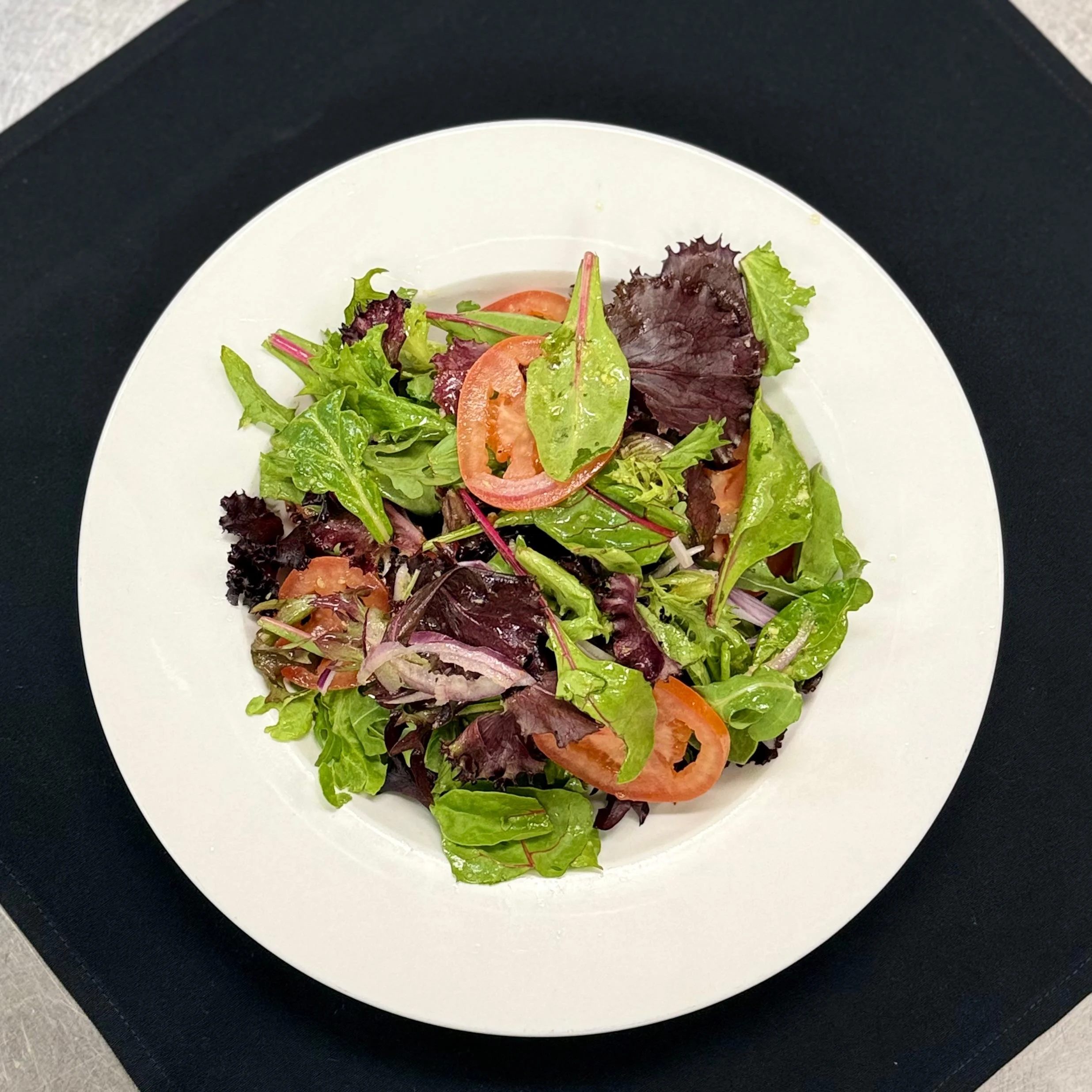 A fresh salad with mixed greens and slices of tomato arranged in a white bowl.