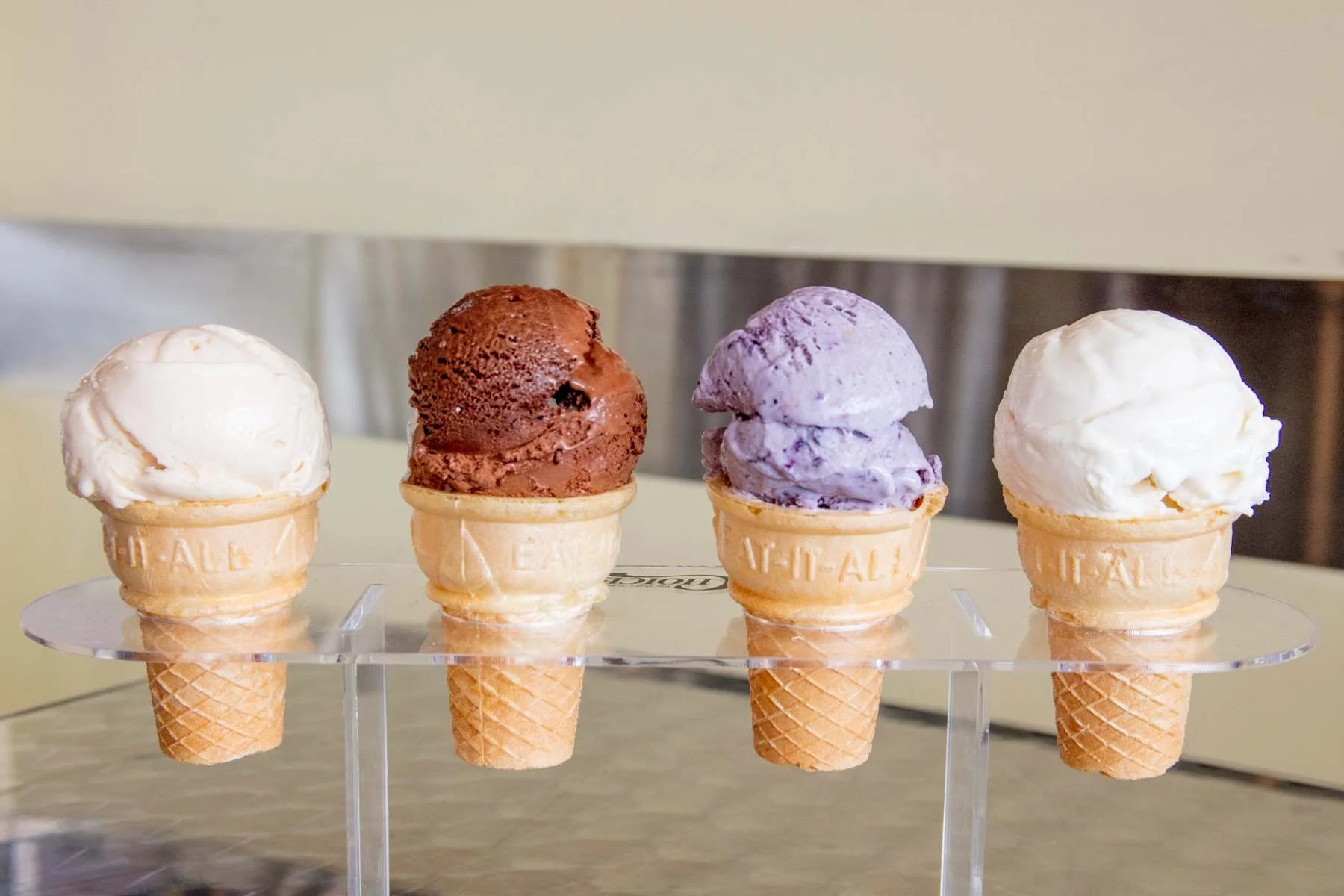 Handcrafted ice cream cones from Hugs Ice Cream in Northwest Arkansas, showcasing vanilla, chocolate, blueberry, and caramel scoops in a clear cone holder.