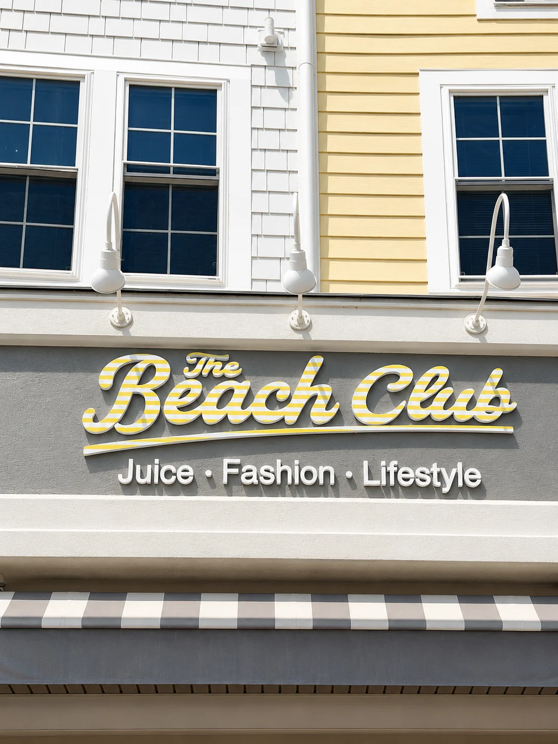 A storefront sign for The Beach Club, advertising juice, fashion, and lifestyle products. The design features a light color palette and modern font.