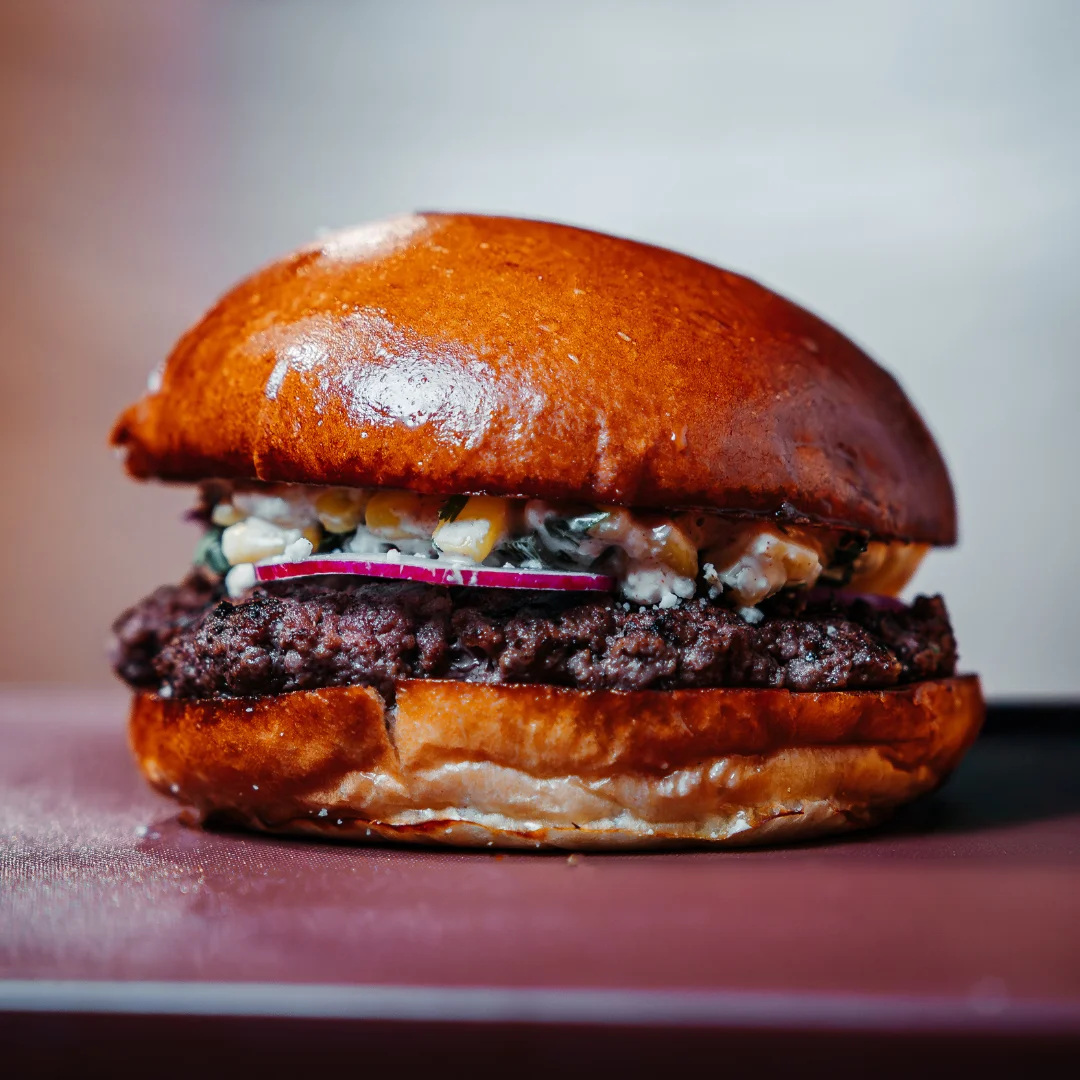A flavorful beef burger topped with a mixture of ingredients, including red onions, in a glossy bun.