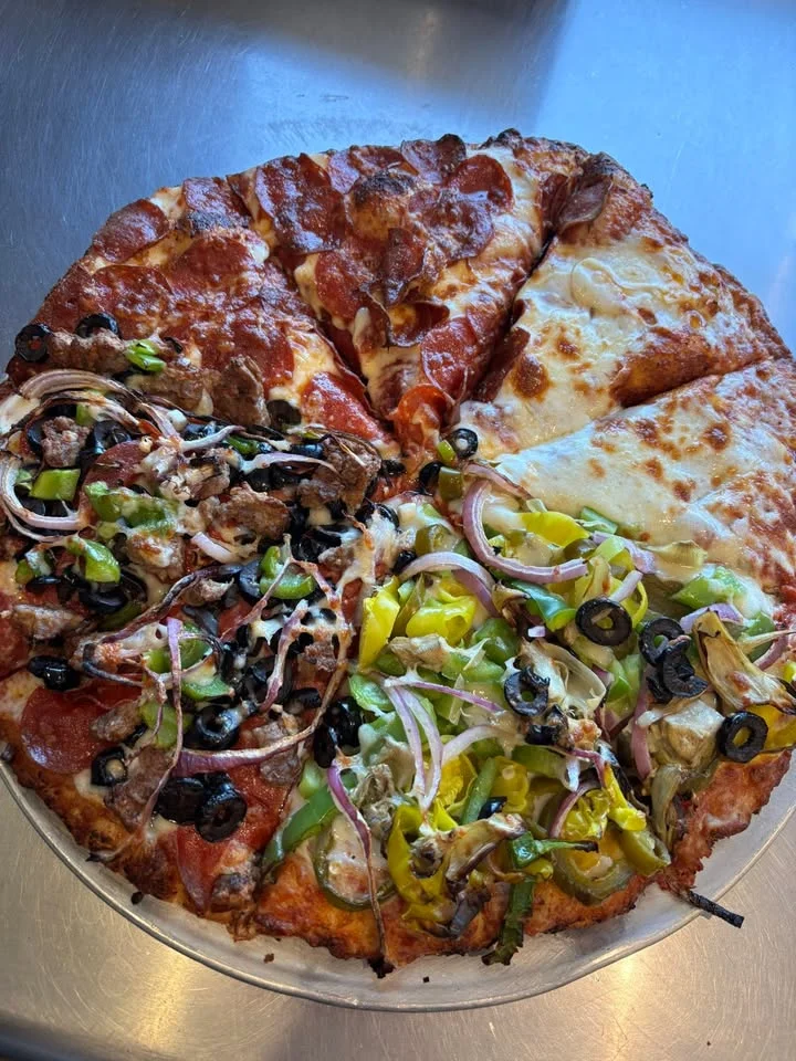 A large pizza sliced into equal sections, featuring toppings of pepperoni, sausage, green peppers, onions, black olives, and a classic cheese slice.