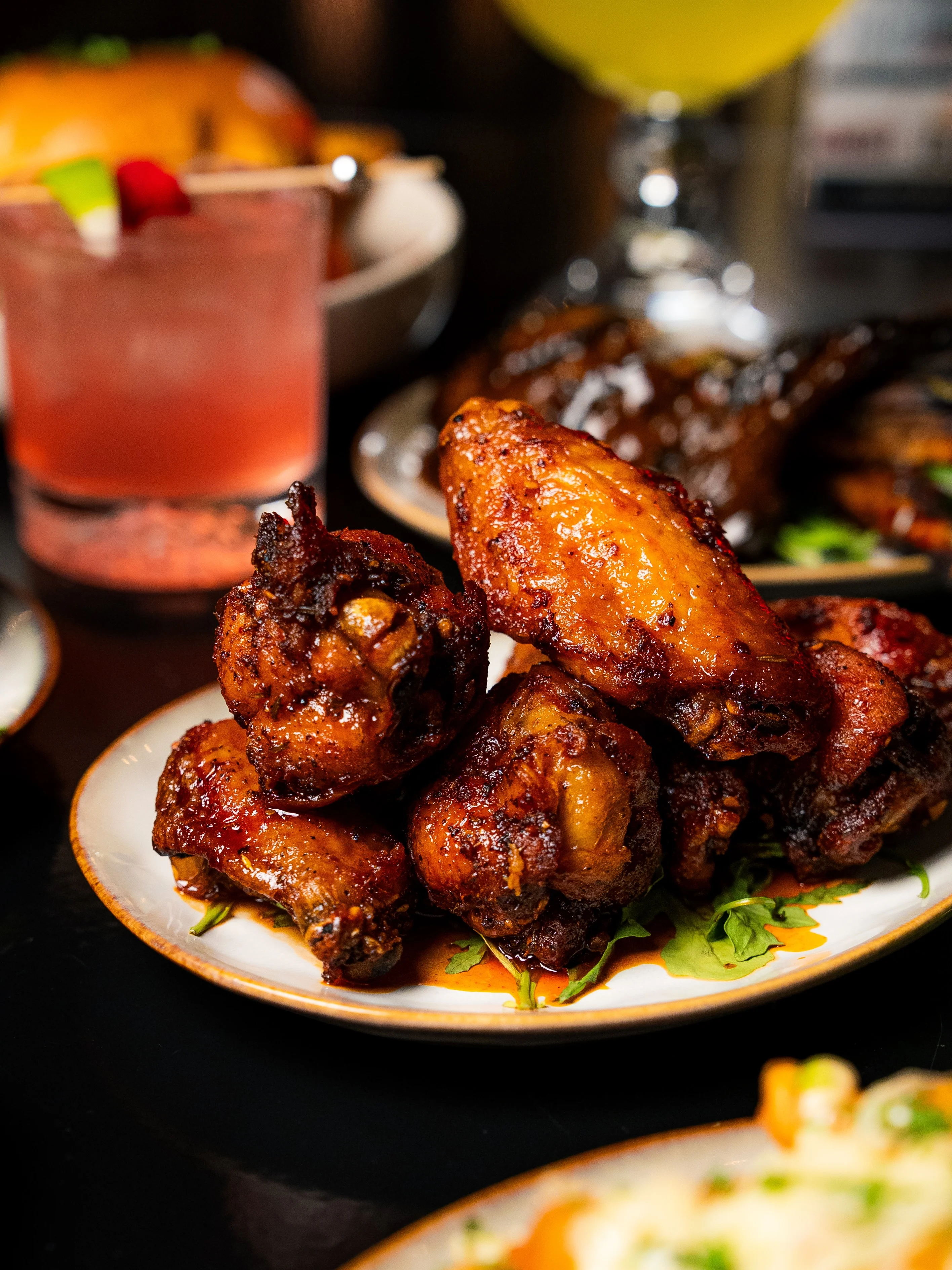 A close-up of a plate featuring several fried chicken wings, glazed with a rich sauce and garnished with green herbs.