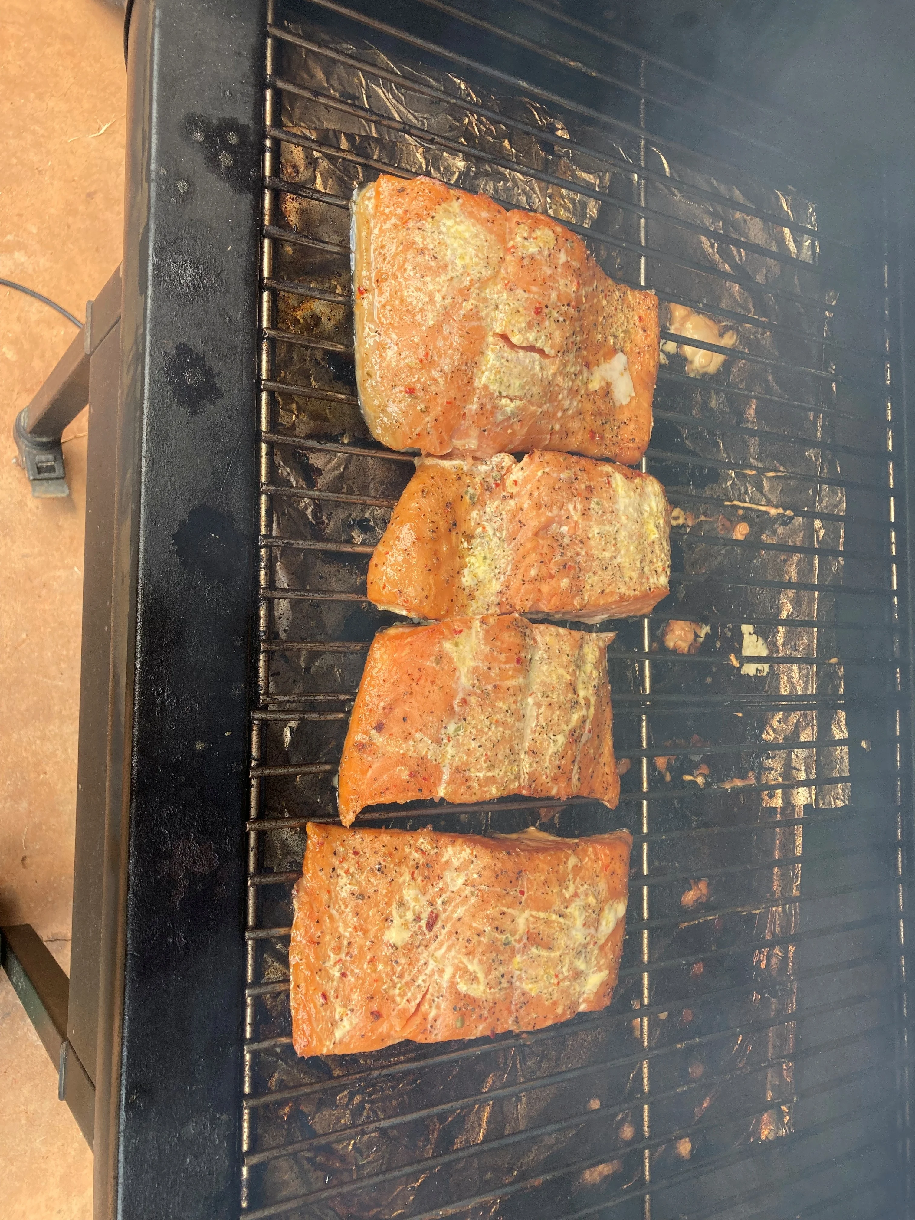 Salmon fillets seasoned and grilling on a barbecue, with smoky aromas filling the air.
