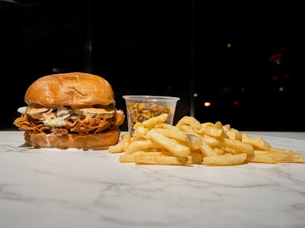 A hearty chicken sandwich accompanied by a small cup of coleslaw and a generous portion of golden fries.