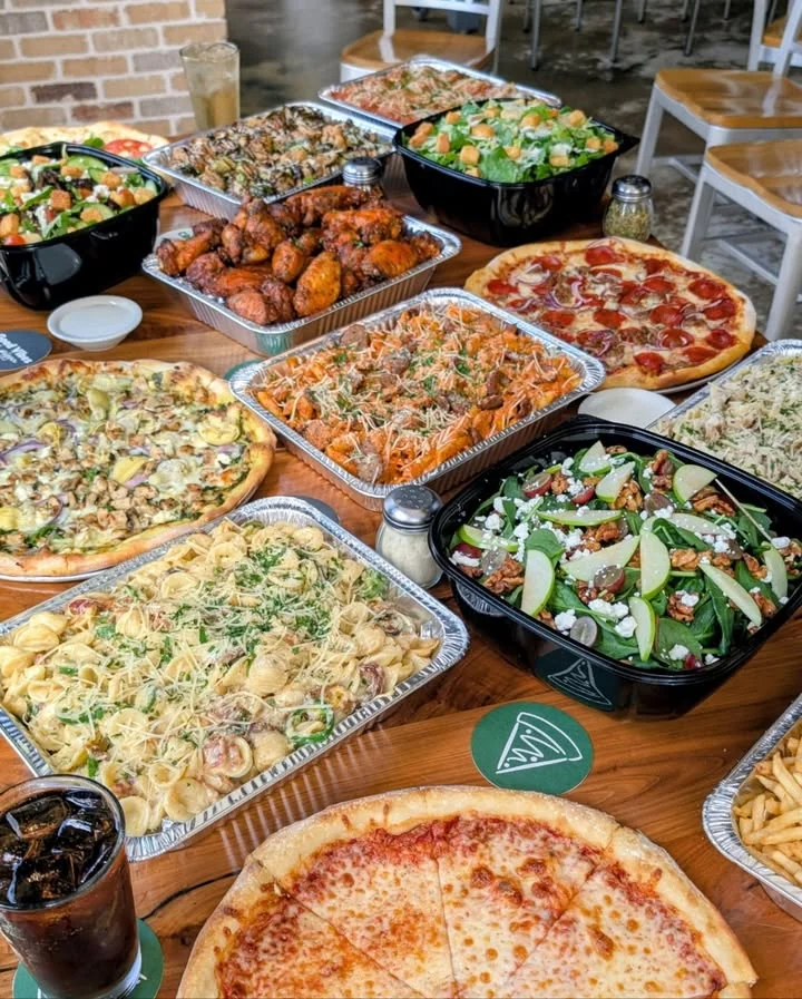 A variety of dishes including salads, pizza, and pasta are spread out on a table, showcasing a feast.