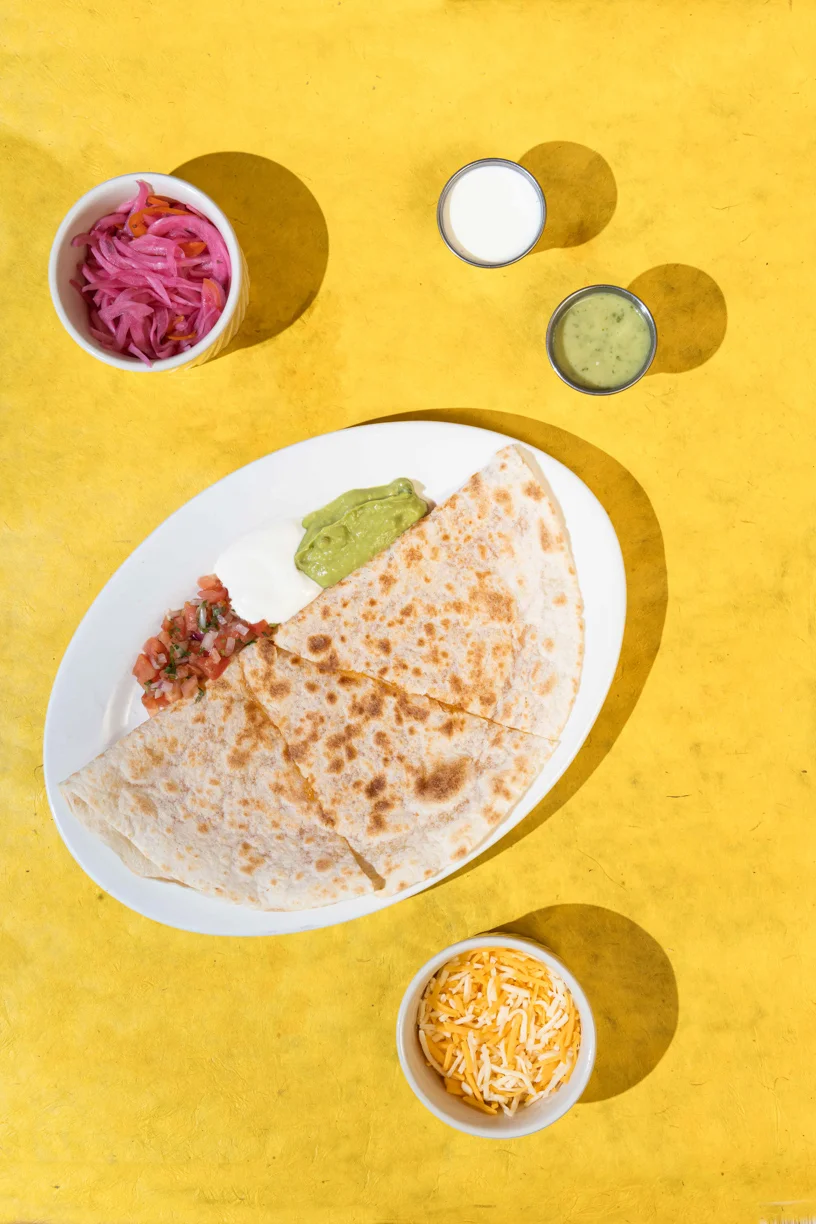 Cheese quesadilla served with guacamole, sour cream, pico de gallo, and a side of shredded cheese at Friducha in Brooklyn, NY.