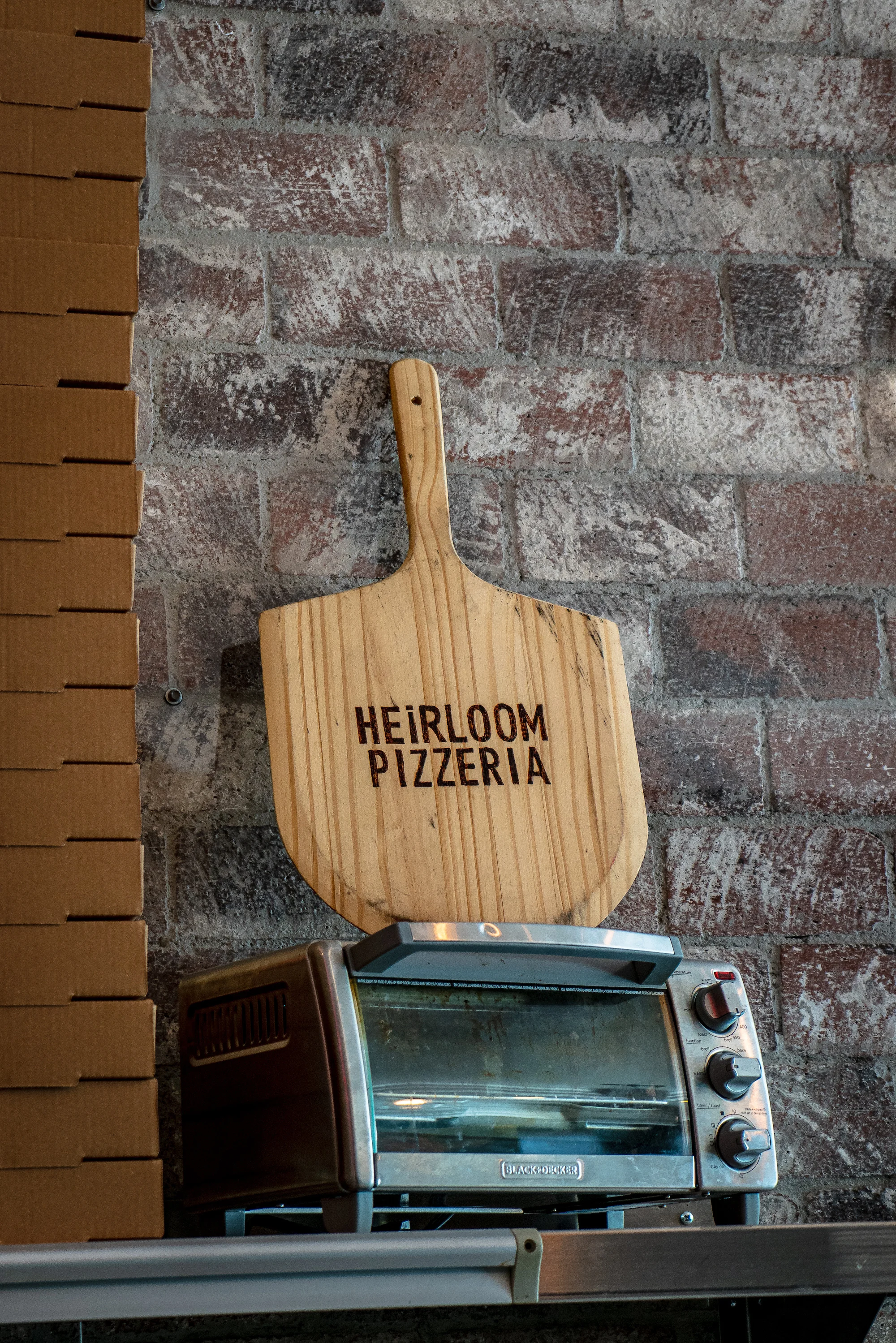 Wooden pizza peel with Heirloom Pizzeria sign on a brick wall