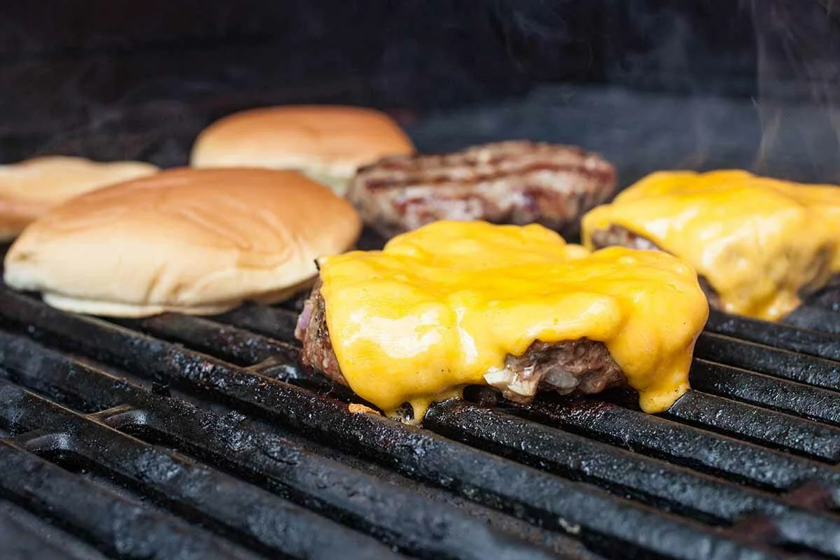 American cheeseburgers grilling with melted cheddar and toasted buns