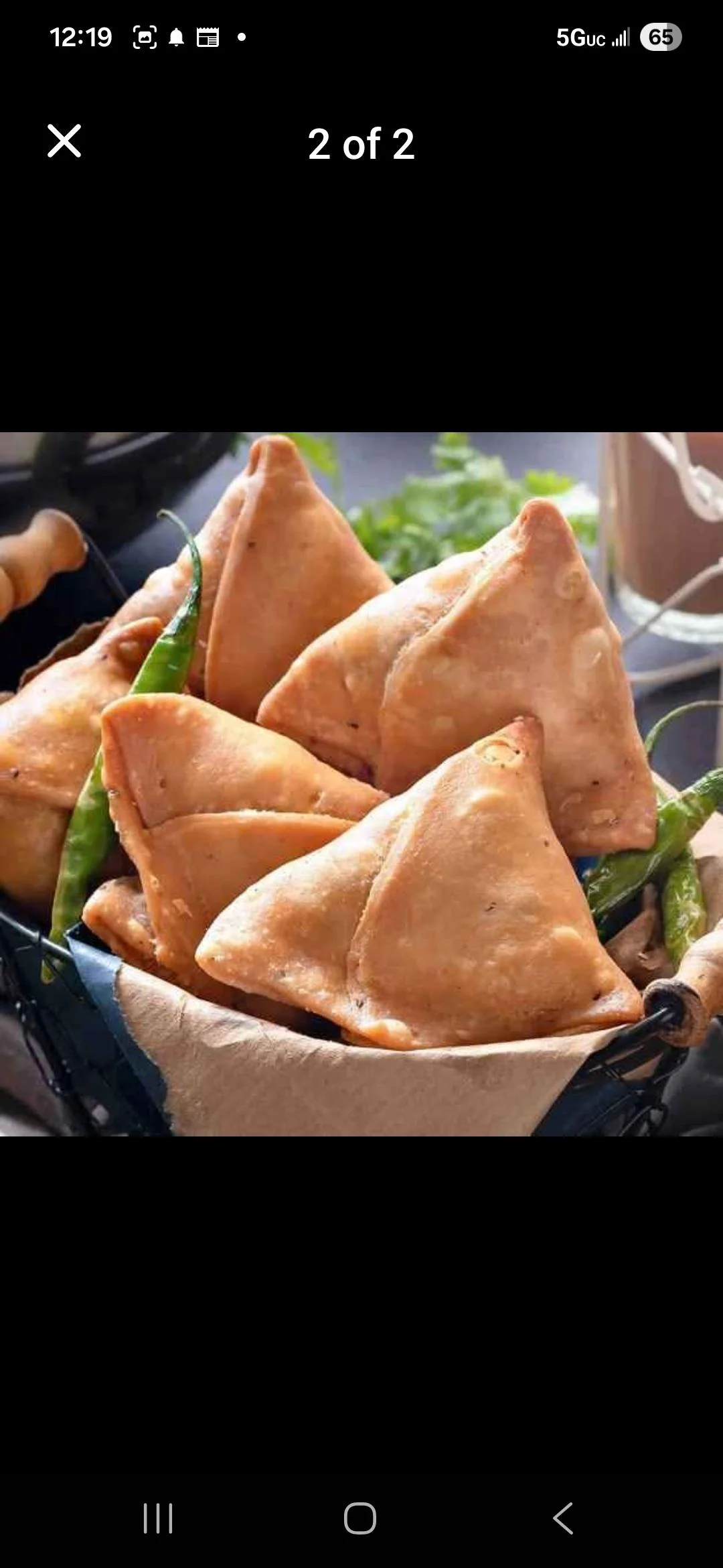 A basket of golden-brown samosas arranged neatly, with some fresh green chilies in the background.