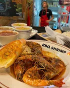 A plate of seasoned BBQ shrimp served with garlic bread and sides, highlighting a delicious seafood dish.