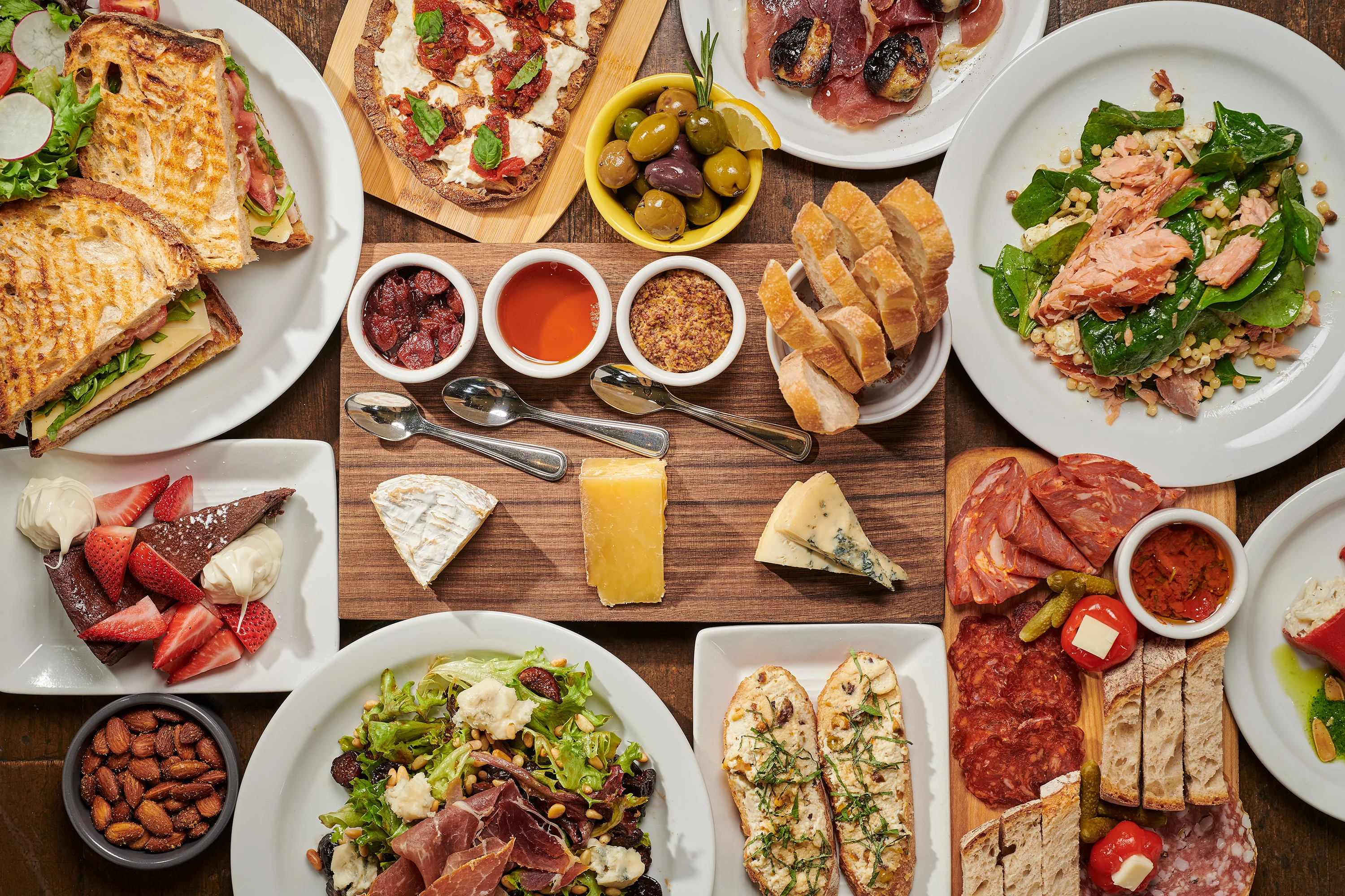 Overhead spread of Italian antipasti, charcuterie, cheeses, salads, and toasted breads