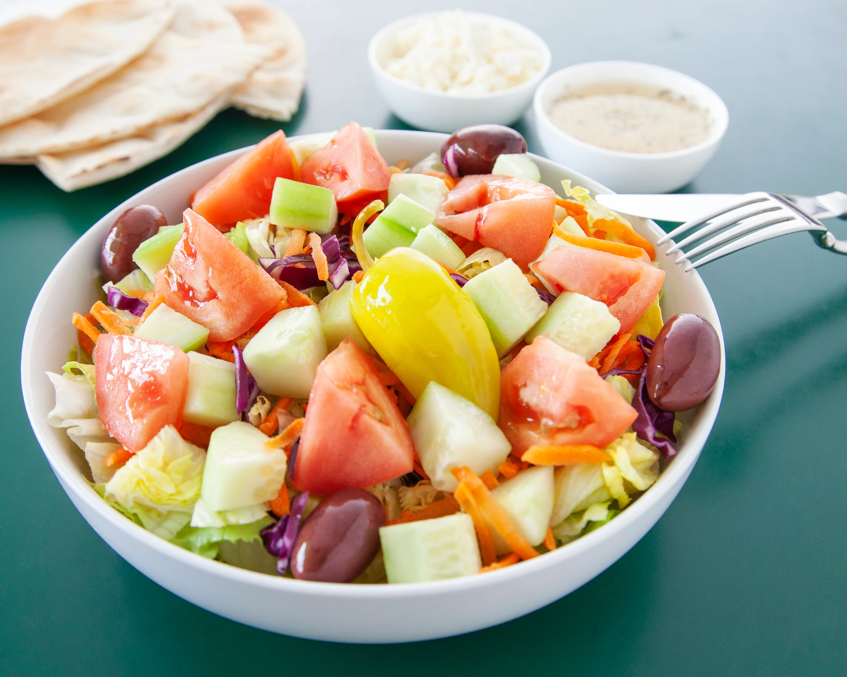 Greek salad platter with pita, hummus, rice, olives, tomatoes, and cucumber