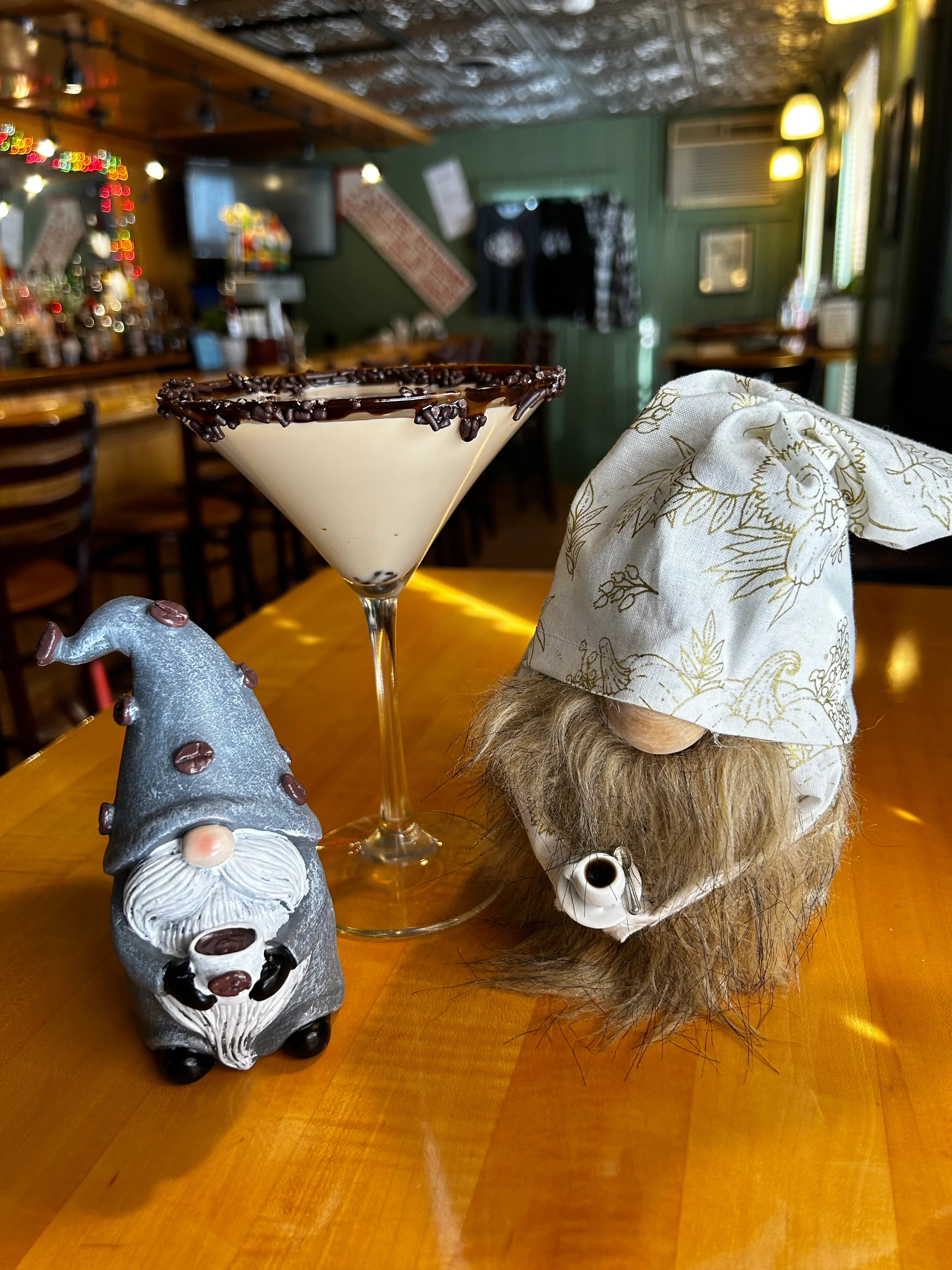 A gnome figurine alongside a chocolate-rimmed martini in a casual dining setting.