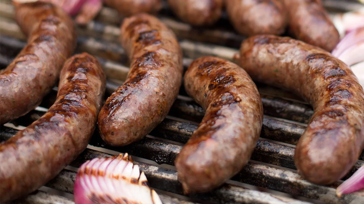 Grilled sausages on a barbecue grill with sliced onions.