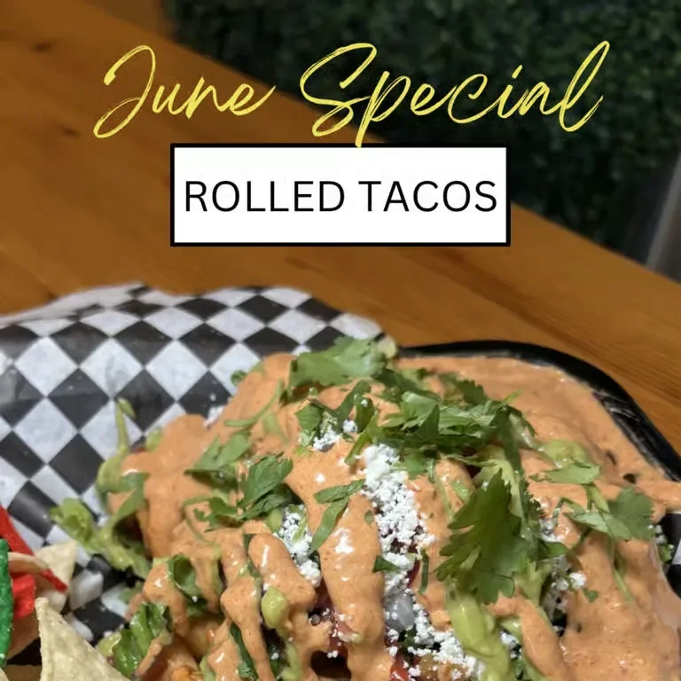 A taco filled with pulled meat, fresh tomatoes, and avocado, served with a side of greens on a wooden plate.