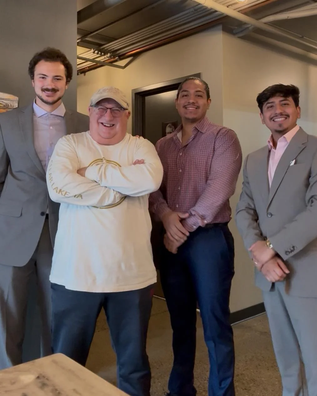 A group of four individuals standing side by side in a casual indoor setting, dressed in business attire.