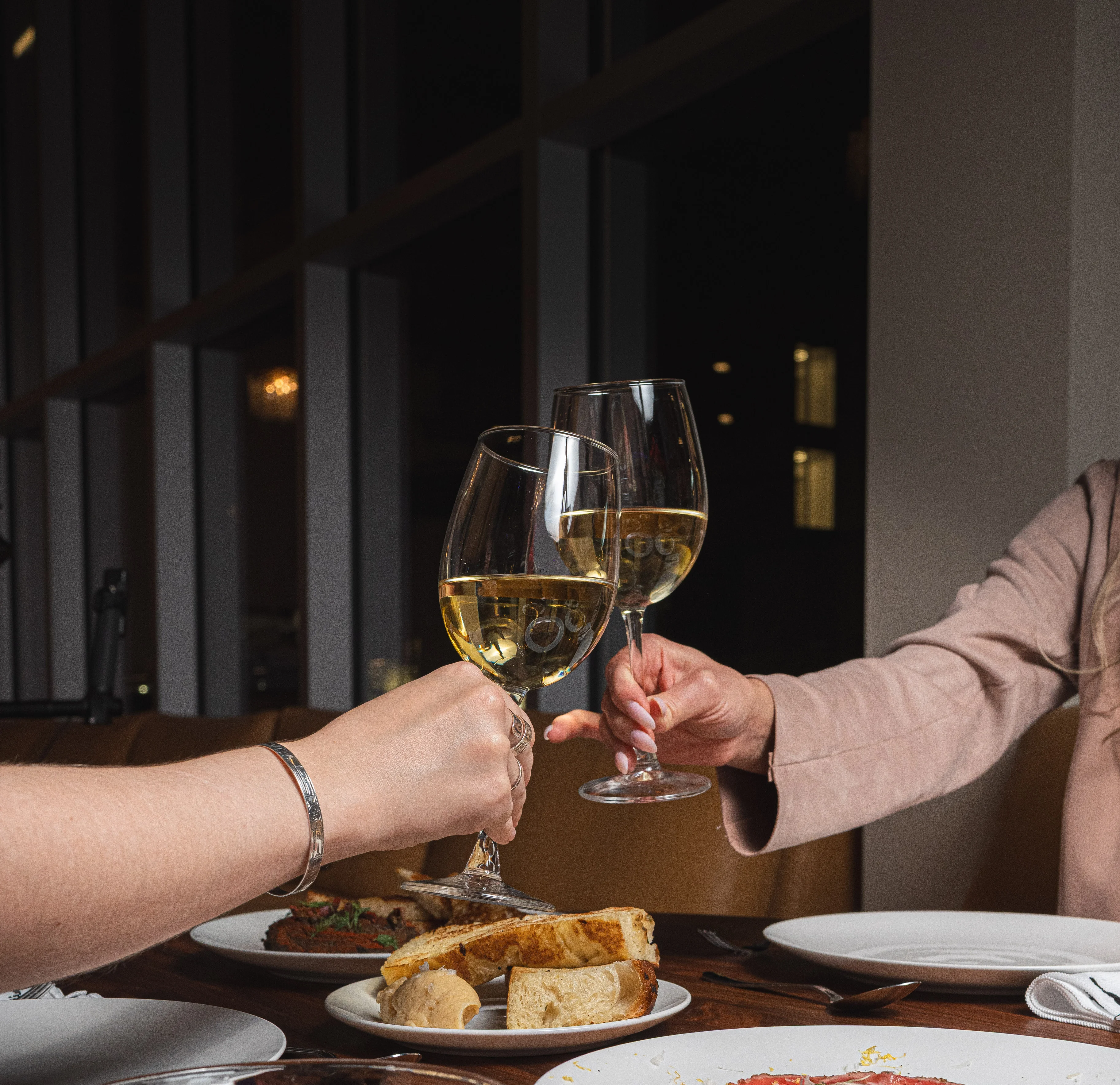 Cheers with white wine glasses at a dining table with various dishes