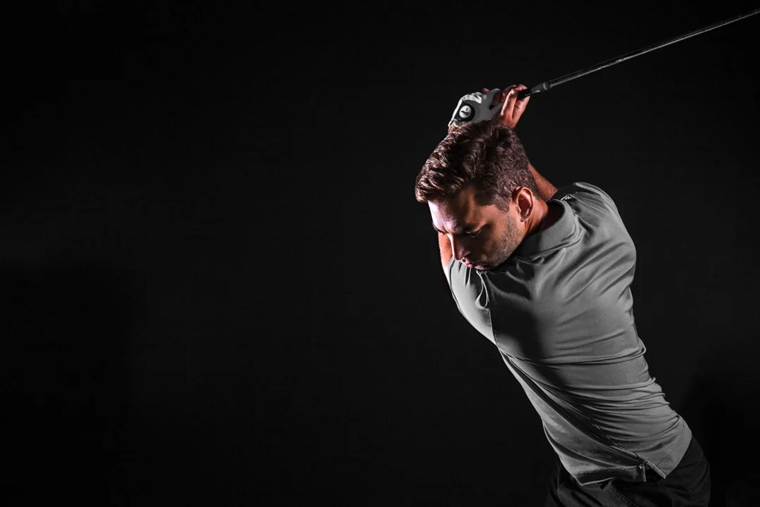 Golfer in action with a driver against a dark background
