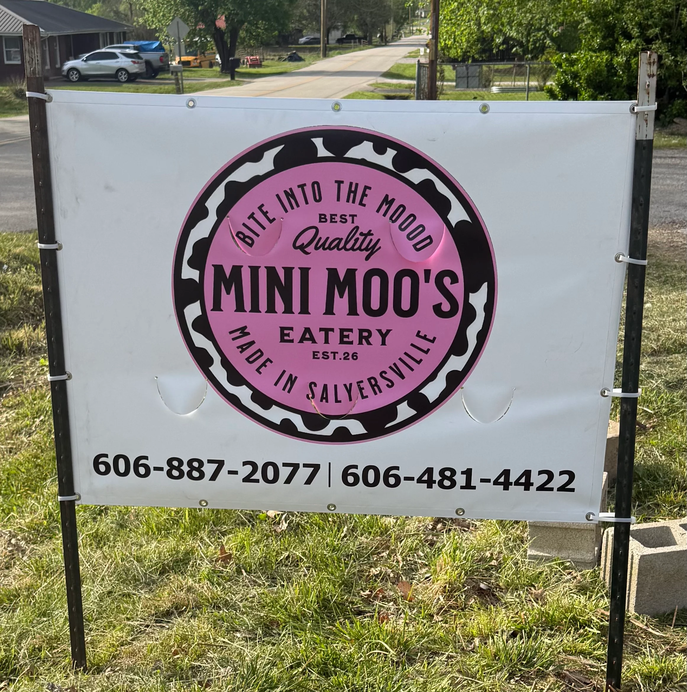 A promotional sign for an eatery featuring a pink and black design, highlighting the establishment's name and contact information.