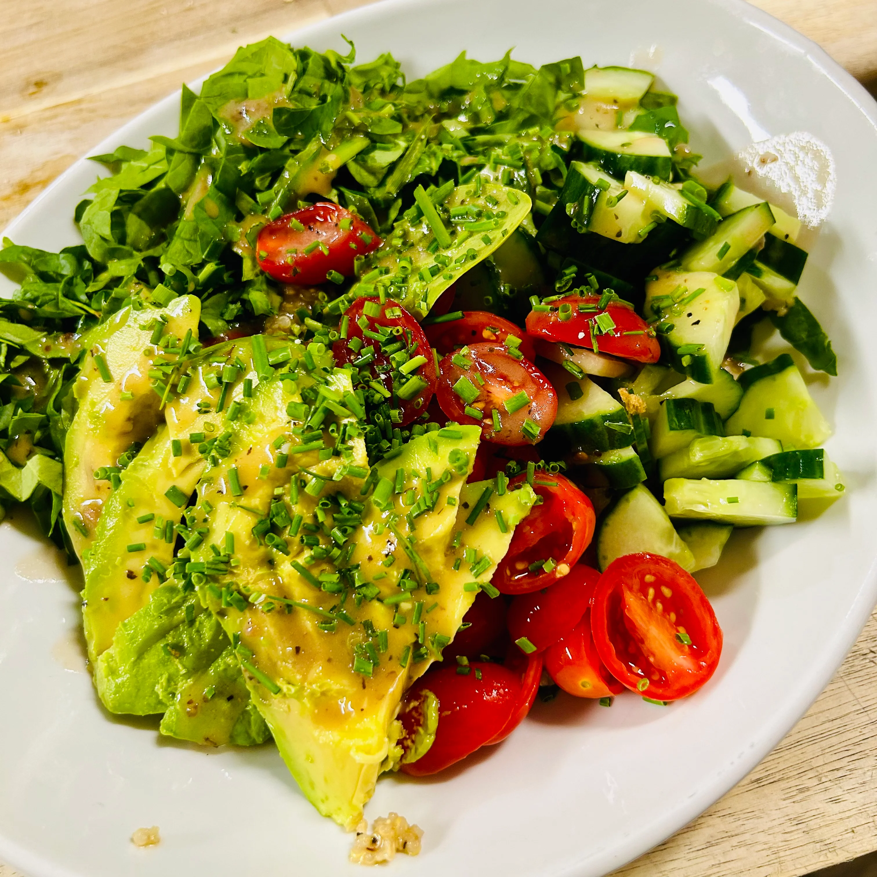 A fresh salad featuring slices of avocado, cherry tomatoes, and cucumber on a bed of greens, topped with chopped chives.