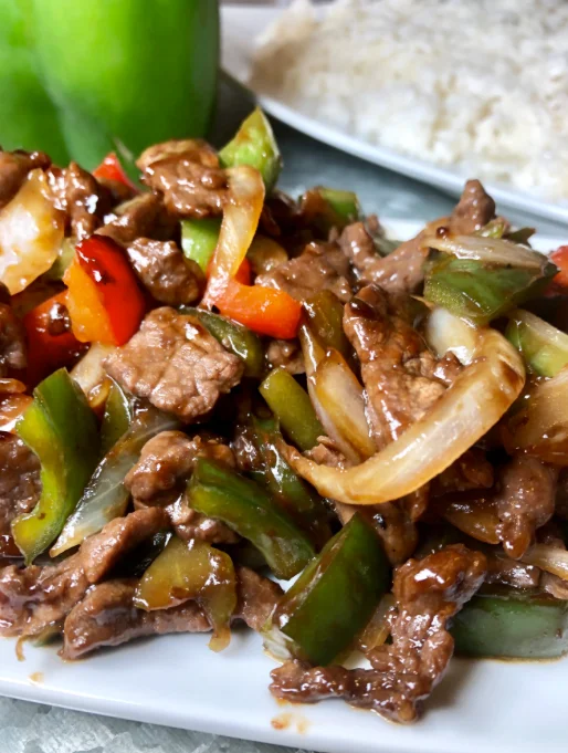 A savory dish of stir-fried beef with colorful bell peppers and onions served with a side of rice.