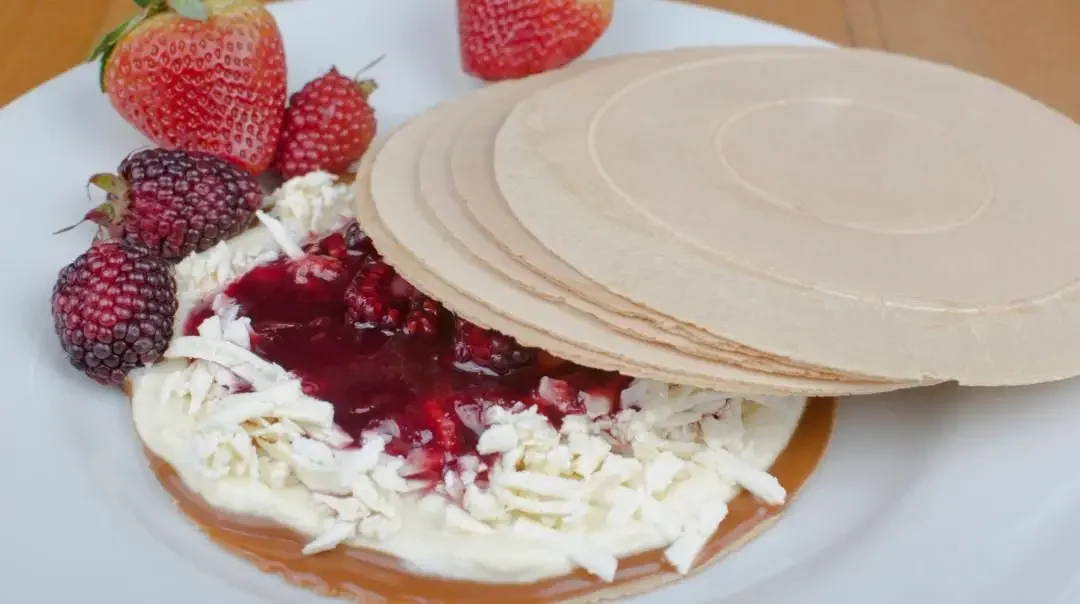 A dessert presentation with thin wafers stacked beside a creamy mixture topped with fruit preserves, accompanied by fresh strawberries and berries.