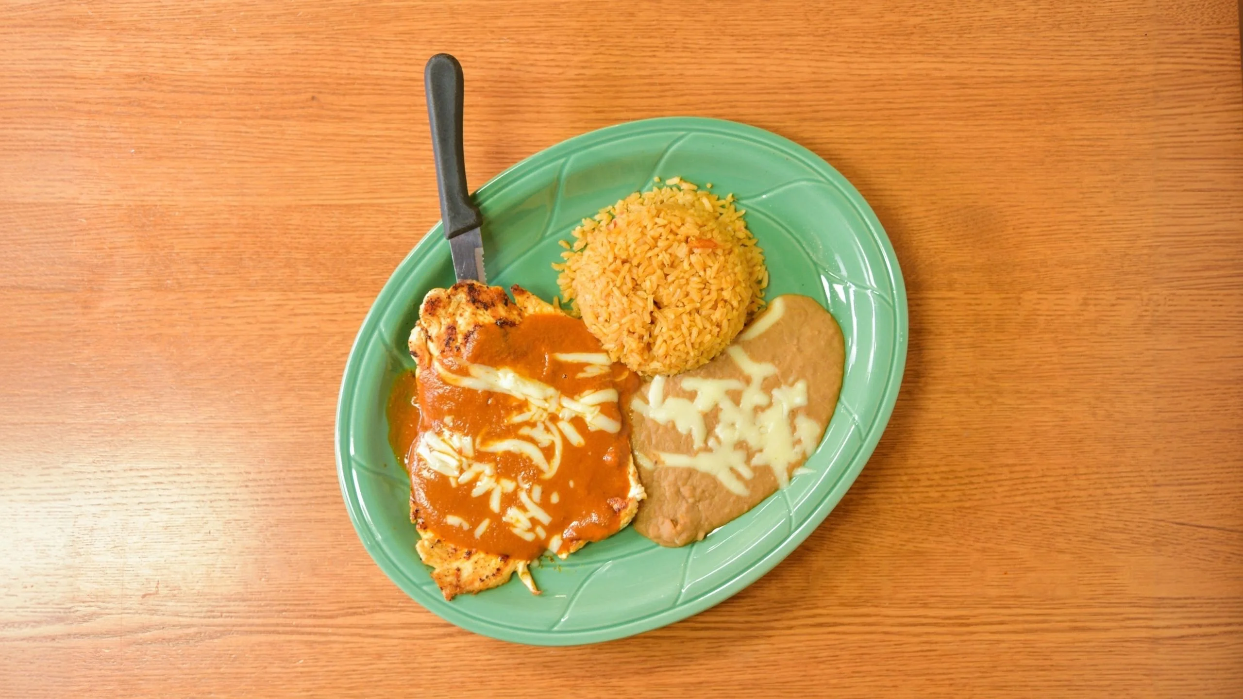 Plate of Mexican chicken enchiladas with rice and refried beans