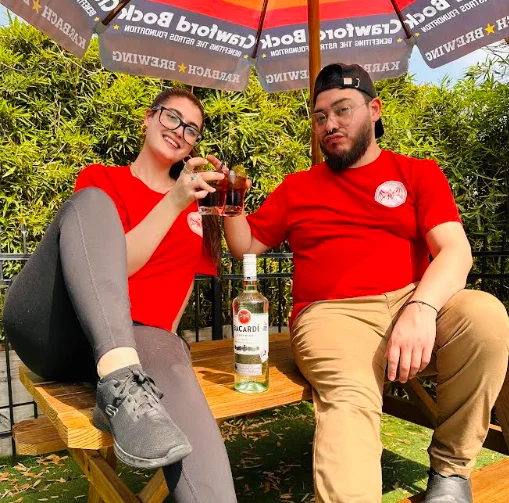 Two friends toasting with drinks under a colorful umbrella