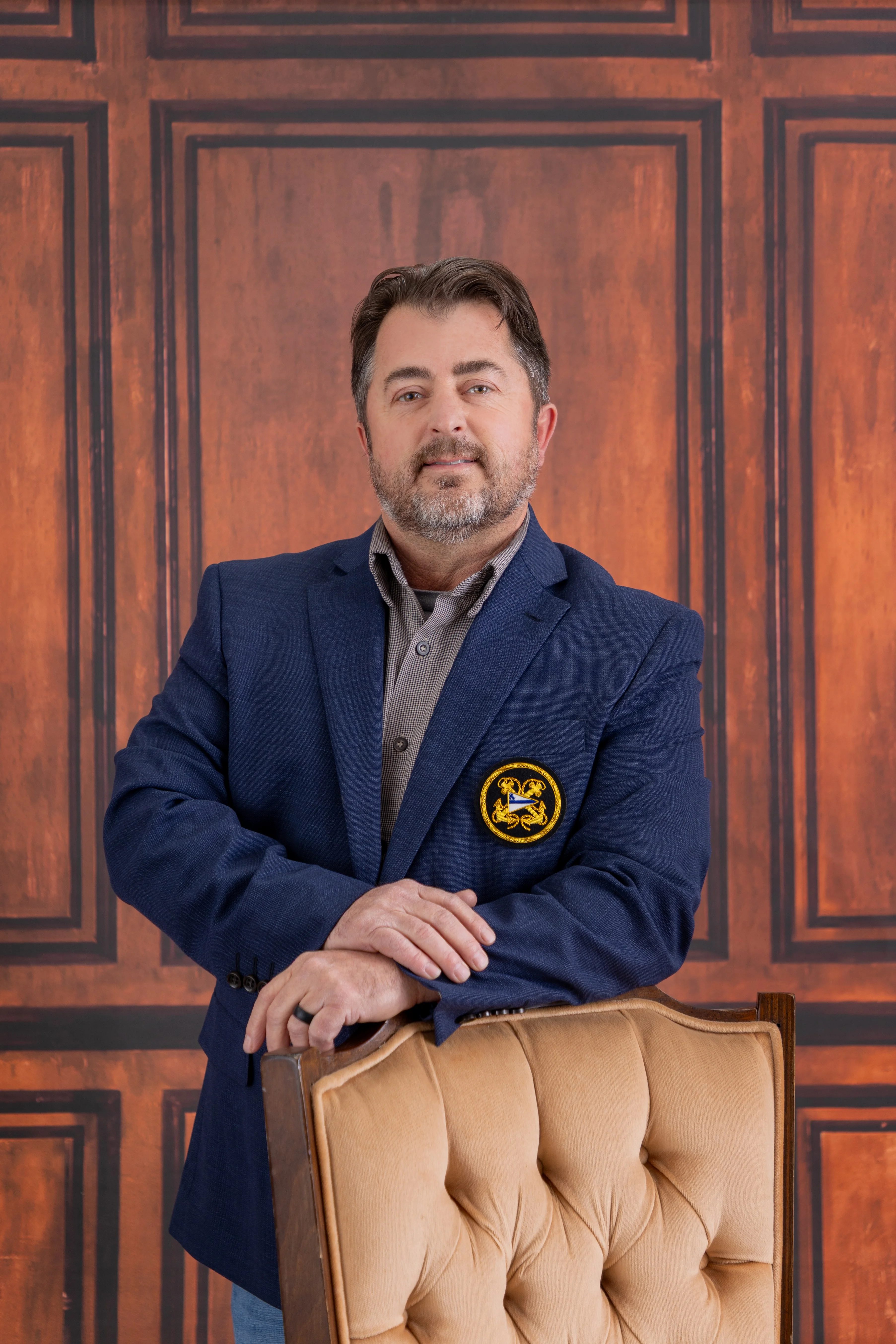 Professional portrait of a man in a blue blazer with a wooden backdrop