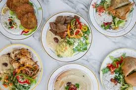 A variety of Mediterranean meals displayed on multiple plates, featuring salads, meats, and colorful garnishes on a marble background.