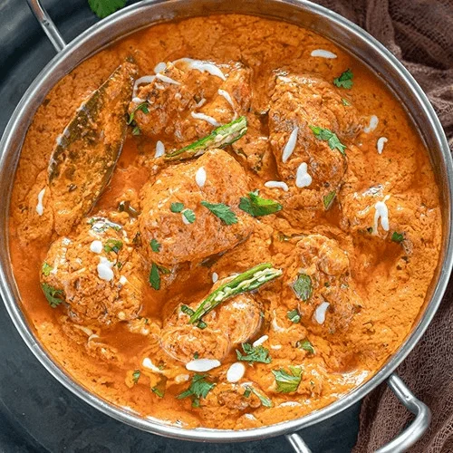 Overhead view of smooth orange butter chicken curry in a copper serving bowl.