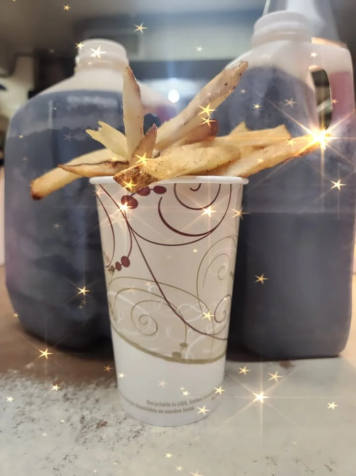 A cup filled with crispy French fries, placed in front of two large containers, with a sparkling effect around the fries.