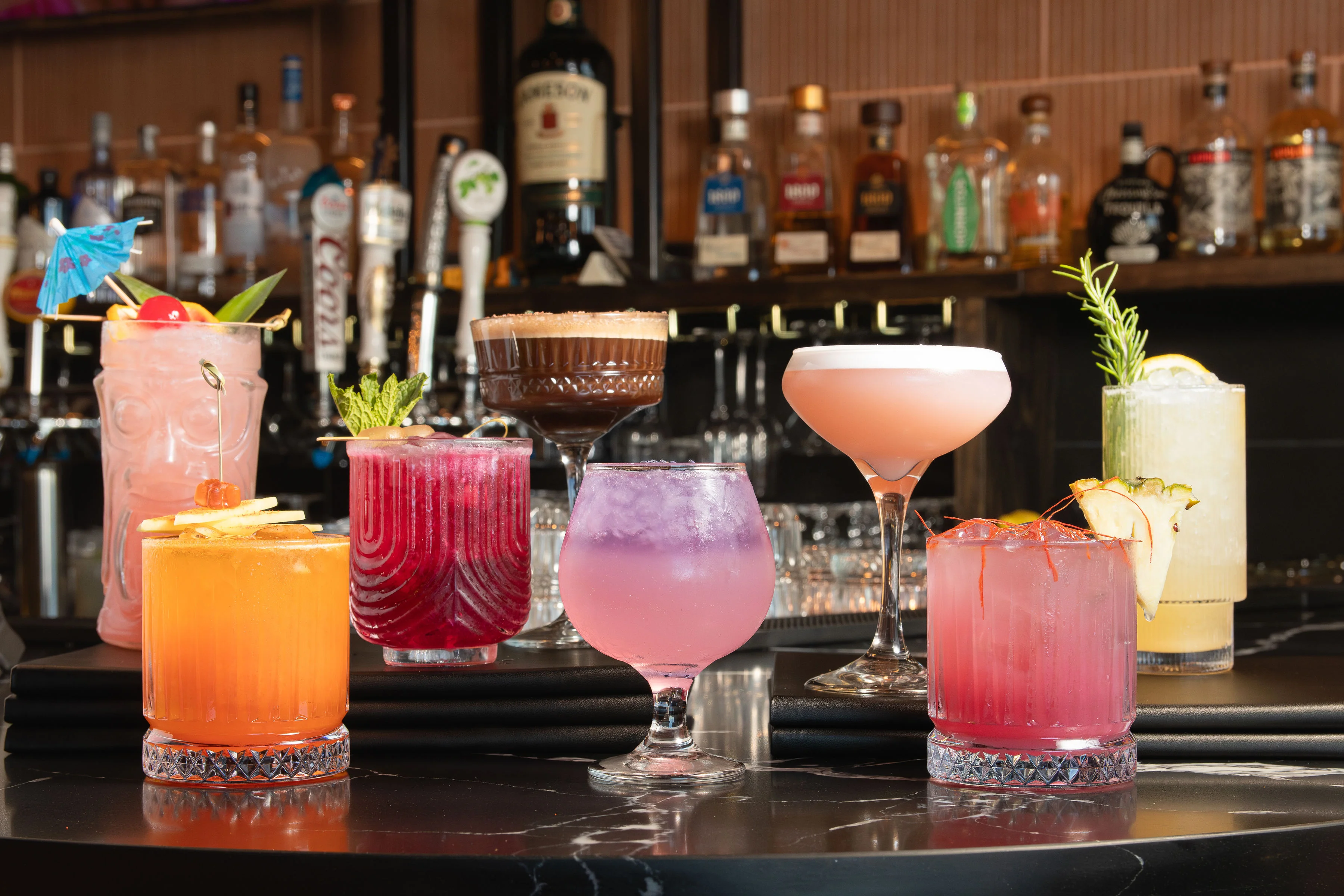 Colorful cocktails displayed on a bar counter with various garnishes.