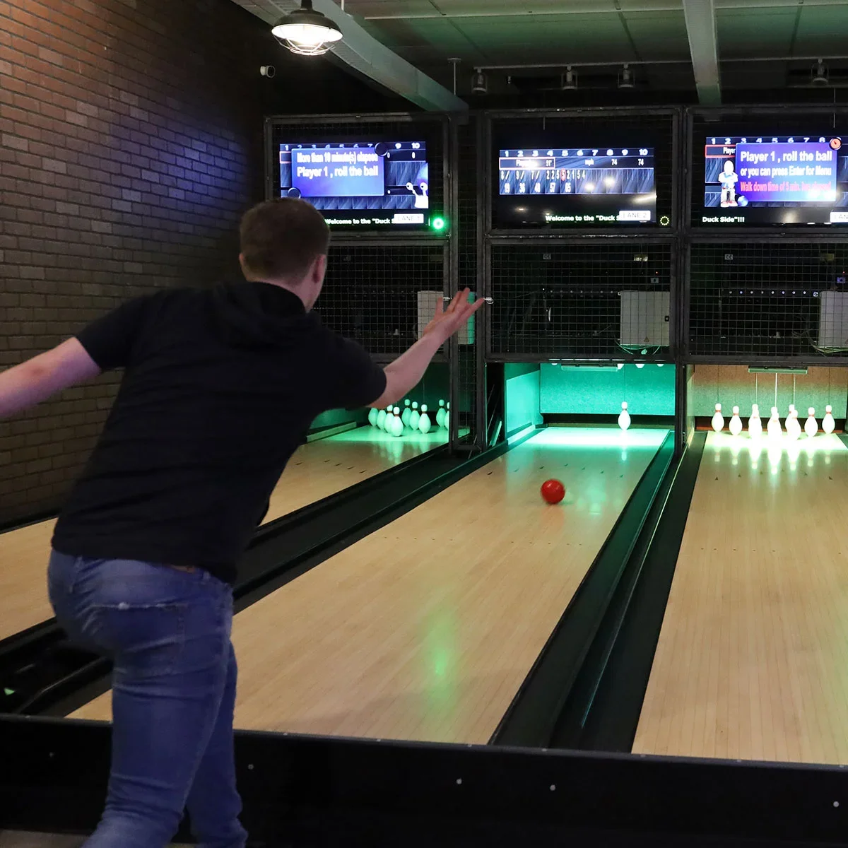 Bowling alley with player rolling a red ball towards pins