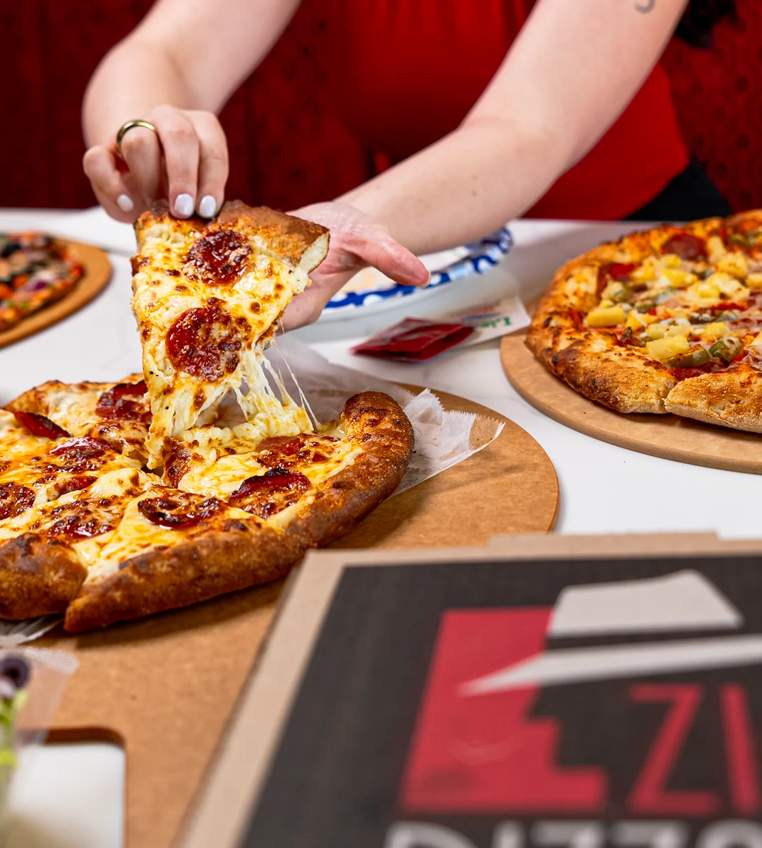A hand reaching for a slice of pepperoni pizza with melted cheese.