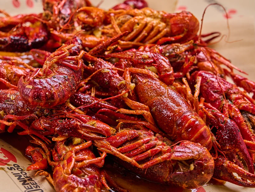 A close-up of spicy boiled crawfish arranged in a large pile. The crawfish are vibrant red and appear flavorful with seasoning.