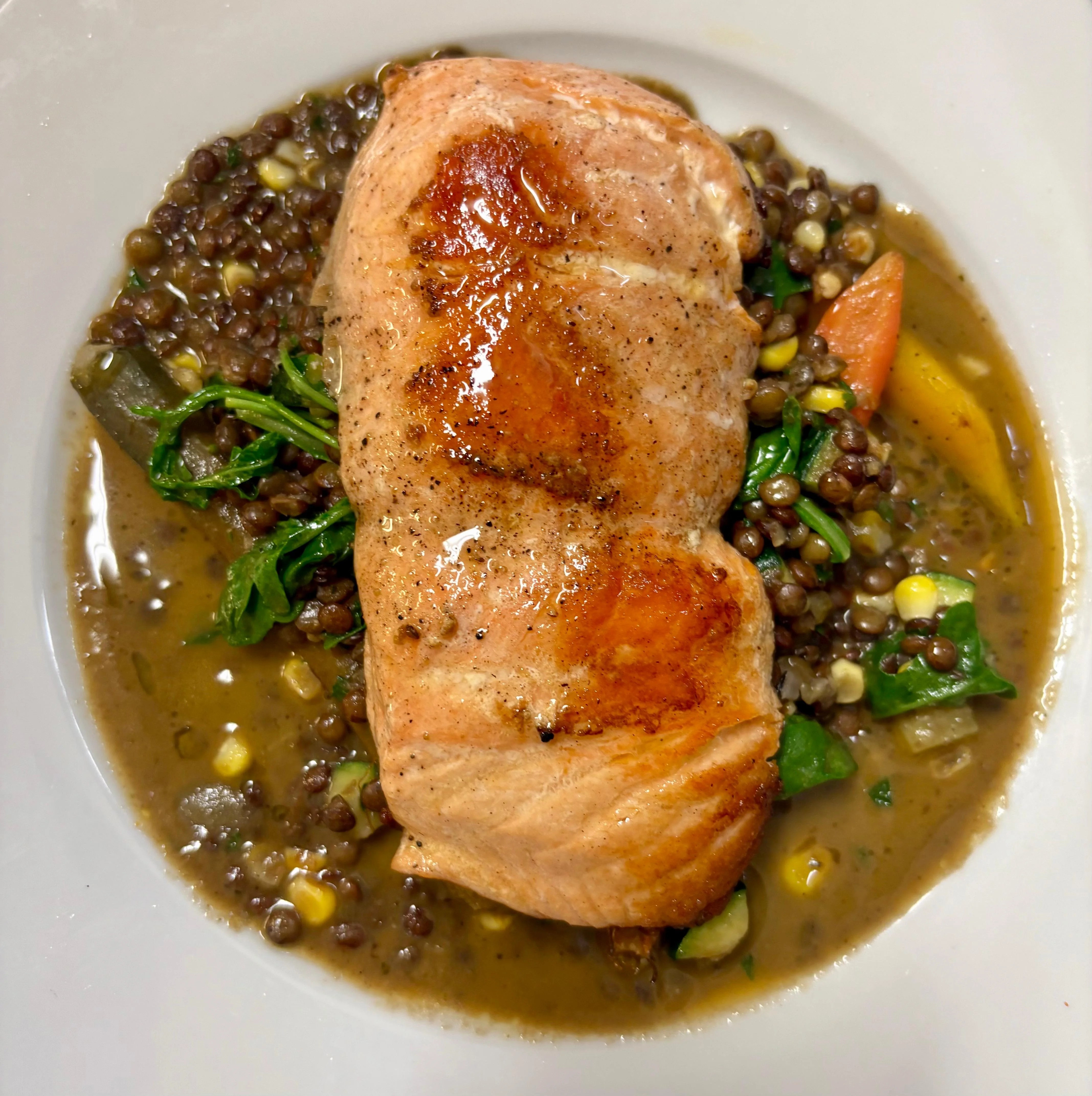 A succulent salmon fillet served on a bed of lentils and mixed vegetables in a savory broth.