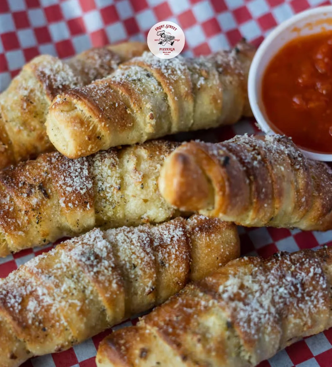 A delicious serving of breadsticks coated in garlic and parmesan cheese, served with a side of marinara sauce. The breadsticks are arranged on a red and white checkered paper.