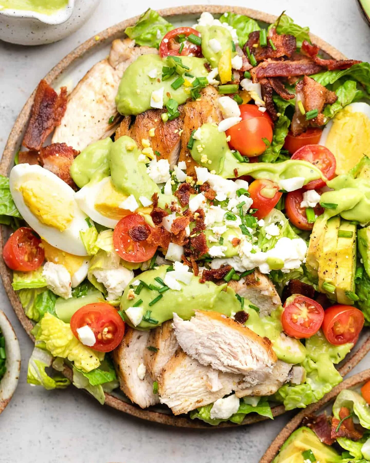 A colorful salad bowl filled with grilled chicken, tomatoes, avocado, hard-boiled eggs, and a creamy dressing.