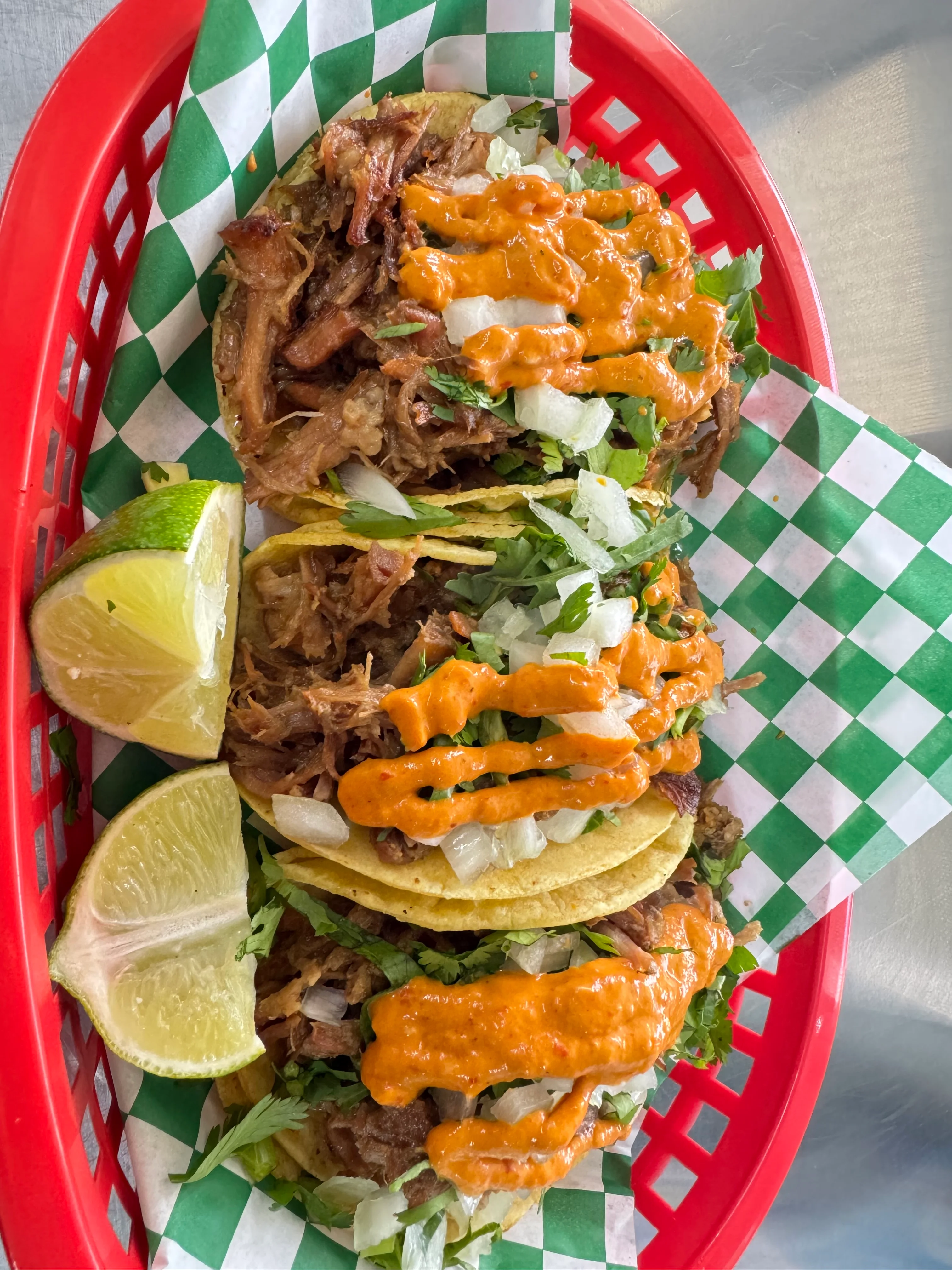 A vibrant dish of tacos filled with shredded meat, topped with sauce, onions, and cilantro, served with lime wedges in a red basket.