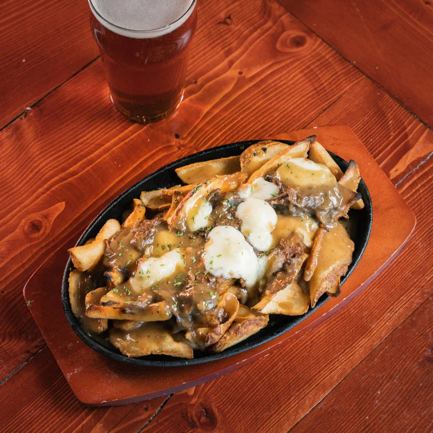 Poutine with gravy and cheese curds served in a sizzling skillet