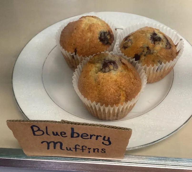 Three blueberry muffins placed on a decorative white plate. Each muffin appears golden brown with blueberries visible on top.