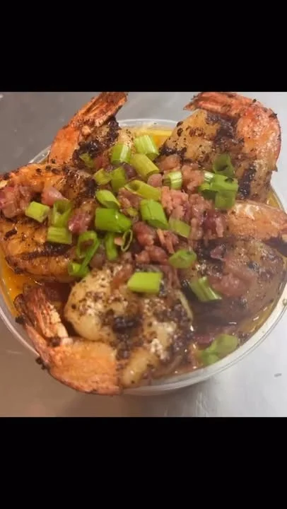 A close-up of a bowl filled with grilled shrimp, garnished with green onions and crispy bits of bacon.