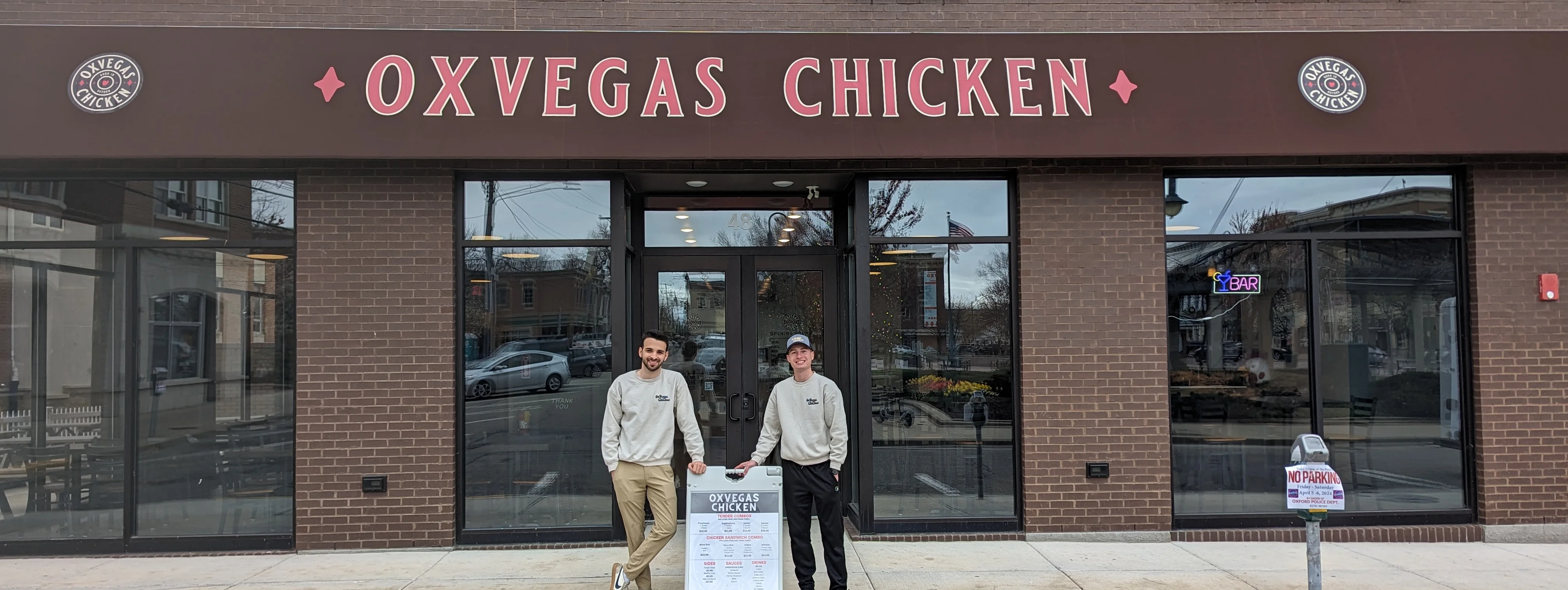 Exterior view of Oxvegas Chicken restaurant with staff and menu sign